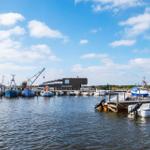 Hafen mit Booten und modernem Gebäude unter blauem Himmel.