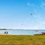 Kitesurfen am Strand mit mehreren Kites im Himmel und Personen im Wasser.