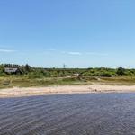 Strand mit Grünflächen und Häusern im Hintergrund unter blauem Himmel