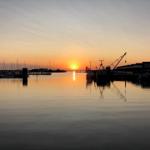 Sonnenuntergang über Hafen mit Booten und Kränen