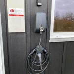 Elektrischer Ladepunkt an der Wand mit aufgerolltem Kabel und Schild.