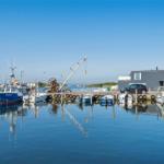 Hafen mit Booten, Krane und modernem Haus an der Wasserkante.