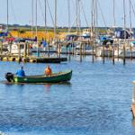 Ein grünes Motorboot fährt durch einen Hafen mit vielen Segelyachten.