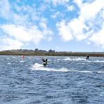 Kitesurfer auf dem Wasser unter blauem Himmel mit weißen Wolken.
