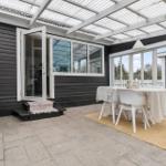 Außenbereich mit Tisch, Stühlen und Grill neben einem Haus mit weißen Fenstern.