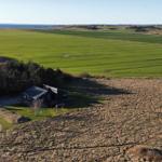 Moderne Villa mit Holzterrasse, umgeben von Feldern und Bäumen.