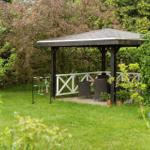 Gartenhütte mit Tisch und Stühlen, umgeben von Gras und Bäumen.