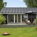 Schwarzes Haus mit Terrasse, Sitzgelegenheiten und Feuerkessel im Garten.