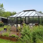Gartenhaus mit Glasdach und Sitzgelegenheiten im Garten.