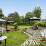 Hinterhof mit Terrasse, Grill und Glasveranda. Umgeben von Grün und Bäumen.