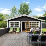 Schwarzes Holzhaus mit Terrasse, Garten und Sitzgelegenheiten.