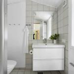 Badezimmer mit Waschbecken, Spiegel, Toilette und Dusche. Fenster mit Blick auf Grün.