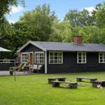 Schwarzes Holzhaus mit Terrasse, Garten und Bänken. Umgeben von Bäumen und Gras.