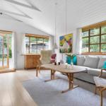 Wohnzimmer mit Sofa, Tisch und Stühlen. Große Fenster und Tür zur Außenterrasse.
