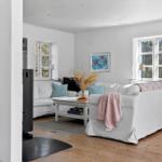 Wohnzimmer mit weißem Sofa, Holzboden und Fenstern. Es gibt einen Kamin und eine Couch.