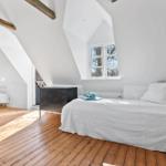 Schlafzimmer mit Dachschrägen, Holzboden und Fenster. Bett, Nachttisch und Lampe sind vorhanden.