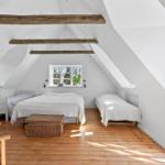 Schlafzimmer mit Dachschrägen, Holzboden und drei Betten. Fenster und Balkonzugang.