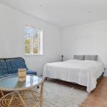 Schlafzimmer mit Bett, Fenster, Tisch und Sitzgelegenheit. Holzwand und Teppichboden.