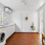 Küche mit Waschmaschine, Fenster und Holzbank. Weiße Wände, Terrakottboden und Haken.