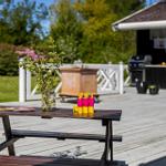 Holztisch mit Blumen und Eisbechern auf Terrasse. Grillhütte und Garten im Hintergrund.