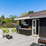 Terrasse mit Grill, Küchenzeile und Liegestühlen neben einem schwarzen Haus.