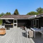 Terrasse mit Tisch, Bänken und Grill. Schwarze Fassade, weißer Zaun und Garten.