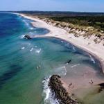 Strand mit klarem Wasser und Sand, Menschen baden und entspannen.