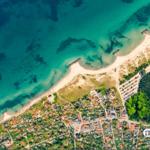 Aerial view of a coastal village with sandy beach, turquoise water, and surrounding greenery.