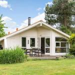 Ein weißes Haus mit Terrasse, Garten und Bäumen. Tisch und Stühle stehen draußen.