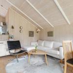 Wohnbereich mit Sofa, Tisch und Stühlen. Holzwände und -decke. Fenster mit Blick draußen.
