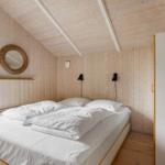Schlafzimmer mit Holzwand, Bett und Fenster zur Außenterrasse.