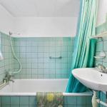 Badezimmer mit Badewanne, Duschbrause und Waschbecken mit grüner Fliesenwand.
