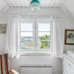 Schlafzimmer mit Dachfenster, Blick aufs Meer, weiße Wände und Vorhänge.