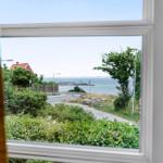 Durch das Fenster blickt man auf eine Straße, Grünflächen und das Meer.
