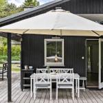 Terrasse mit weißem Tisch, Stühlen und Sonnenschirm. Schwarze Holzwände und offene Tür.