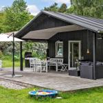 Schwarze Holzhütte mit Terrasse, Grill, Sitzgruppe und Kinderspielwasserbecken im Garten.