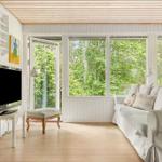 Wohnzimmer mit Sofa, Fernseher und Blick auf grüne Bäume durch große Fenster.
