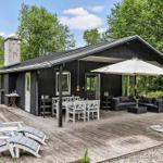 Schwarzes Haus mit Holzterrasse, Gartenmöbeln und Sonnenschutz. Umgeben von Bäumen und Grün.