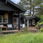 Schwarzes Holzhaus mit Terrasse, Garten und Bäumen. Möbel und Pflanzen sind sichtbar.