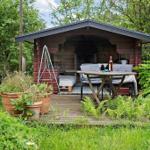 Hölzerner Gartenbau mit Tisch, Stühlen und Grill. Pflanzen und Gras umgeben die Terrasse.