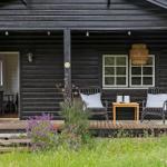 Schwarze Holzhütte mit Terrasse, zwei Stühlen und Tisch. Tür offen, Blick ins Innere.