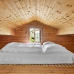 Ein Bett mit weißer Bettwäsche in einem holzverkleideten Raum mit Dachschrägen und einem Fenster.