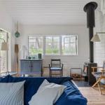 Ein Raum mit blauem Sofa, Holzfußboden und Kaminofen. Fenster, Stühle und Schrank sind sichtbar.