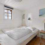 Schlafzimmer mit weißem Bett, Holzboden und Fenster mit Blick nach draußen.