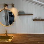 Badezimmer mit runden Spiegel, Holzregalen und goldfarbenem Waschbecken.