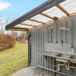 Terrasse mit Esstisch, Whirlpool und Grillplatz. Umgeben von Bäumen und Grünfläche.