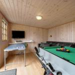 Room with ping pong table, dart and pool table. Wooden walls and ceiling. Black sofa.