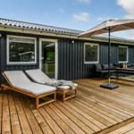 Terrasse mit Sonnenschirm, Liegestuhl und Sitzgruppe vor einem Haus mit dunkler Fassade.
