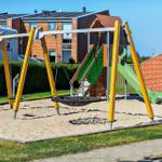 Kinderspielplatz mit Schaukel, Rutsche und Sandkasten vor Wohnhäusern.