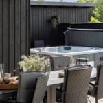 Terrasse mit Tisch, Stühlen und Grill. Blick auf grünes Feld und Haus.
